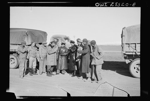 Russian officers in black leather coats surrounded by a group of American soldiers, truck drivers at a dumping spot for supplies which the Americans brought through the Persian corridor. This was one of the first all-American convoys to make the trip bringing aid to Russia. Somewhere in Iran
