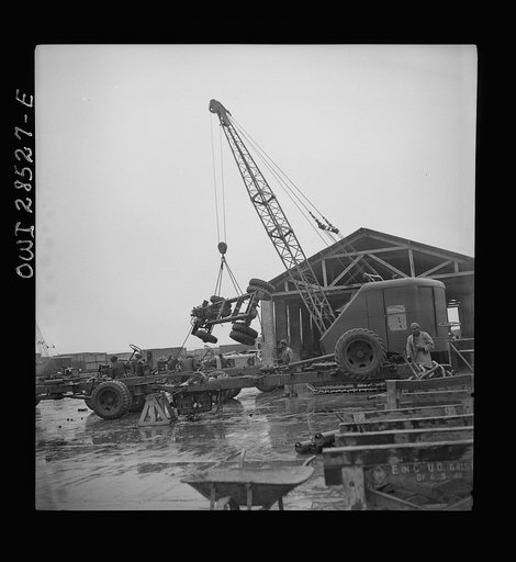 A derrick moving a chassis as the men work ankle deep in water at an American truck assembly plant somewhere in Iran
