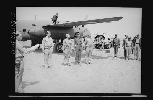 An Allied airbase somewhere in Nothern Africa. Four American airmen of the Bombardment Group, United States Army, Ninth Air Force, take just enough time out to receive their citations while their bonber is being refueled. They are shown as they lined up beside their B-24 just before General Auby C. 