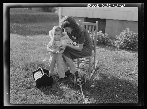 A mother sewing a button on her child's overalls. Silver Spring, Maryland
