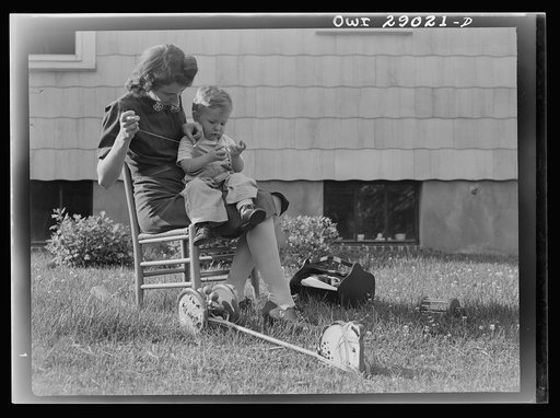 A mother sewing a button on her child's overalls. Silver Spring, Maryland