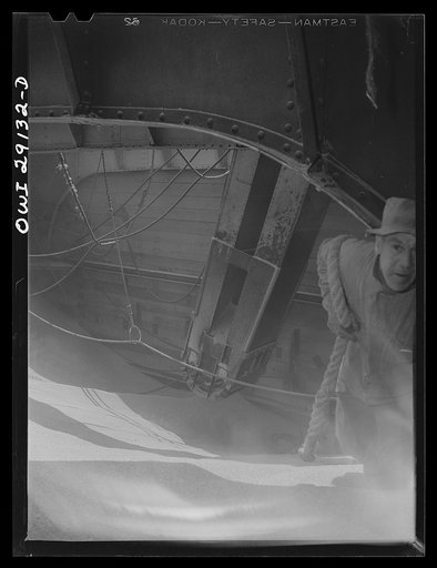 Untitled photo, possibly related to: Buffalo, New York. Half-empty hold of a grain boat from Deluth unloading wheat at a grain elevator on the Erie Canal. In middle ground is the "leg" which draws grain into the tower by means of an endless belt of buckets
