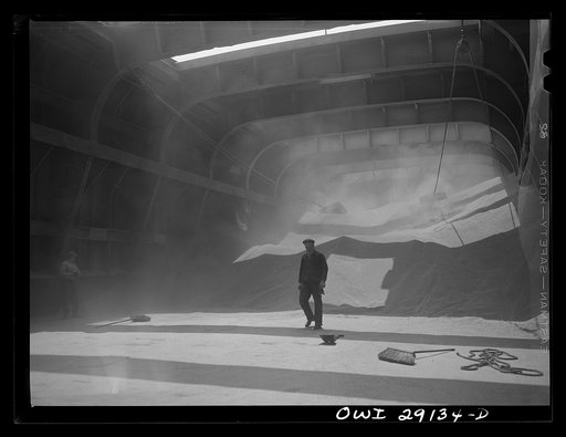 Untitled photo, possibly related to: Buffalo, New York. Inside the half-empty hold of a grain boat from Duluth which is unloading wheat at a grain elevator for the Erie Canal. In the extreme background the "leg" draws wheat into the tower by means of an endless belt of buckets. A shovel rigged up on