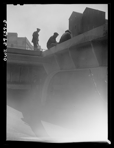 Untitled photo, possibly related to: Buffalo, New York. Inside the half-empty hold of a grain boat from Duluth which is unloading wheat at a grain elevator for the Erie Canal. In the extreme background the "leg" draws wheat into the tower by means of an endless belt of buckets. A shovel rigged up on