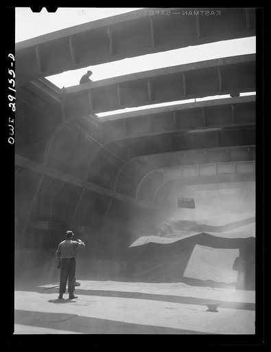 Buffalo, New York. Inside the half-empty hold of a grain boat from Duluth which is unloading wheat at a grain elevator for the Erie Canal. In the extreme background the "leg" draws wheat into the tower by means of an endless belt of buckets. A shovel rigged up on ropes scoops the grain into an area 