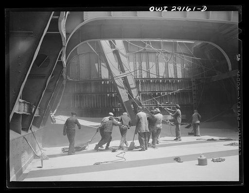 Buffalo, New York. Inside the nearly-emptied hatch of a Duluth grain boat unloading wheat in a grain elevator on the Erie Canal. Men who work here are called scoopers. Here they are guiding the ropes of a shovel which scoops grain into range of the "leg" which draws grain into the tower on an endles