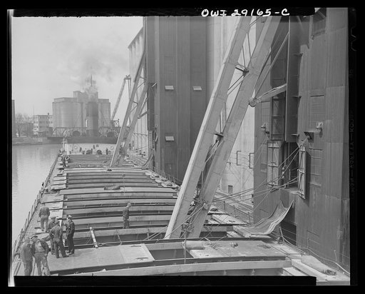 Buffalo, New York. View from the pilot house of a grain boat from Deluth unloading wheat into a grain elevator on the Erie Canal. "Legs" are lowered into the hatches and draw grain into towers on endless belts of buckets