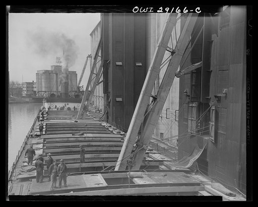 Untitled photo, possibly related to: Buffalo, New York. View from the pilot house of a grain boat from Deluth unloading wheat into a grain elevator on the Erie Canal. "Legs" are lowered into the hatches and draw grain into towers on endless belts of buckets