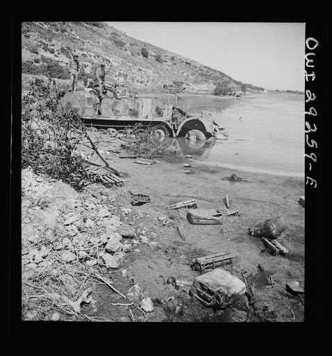 Port Farina beachside strewn with a wide assortment of Nazi military debris and a Nazi half-track in the water