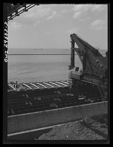 Cleveland, Ohio. Unloading a lake freighter at the Pennsylvania Railroad iron ore docks by means of Hewlett [i.e., Hulett] unloaders. In the foreground, empty cars are waiting to pass under the unloaders to pick up their loads