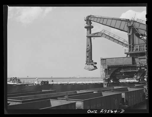 Untitled photo, possibly related to: Cleveland, Ohio. Unloading a lake freighter at the Pennsylvania Railroad iron ore docks by means of Hewlett [i.e., Hulett] unloaders. In the foreground, empty cars are waiting to pass under the unloaders to pick up their loads
