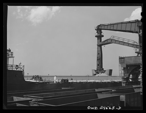 Cleveland, Ohio. Unloading a lake freighter at the Pennsylvania Railroad iron ore docks by means of Hewlett [i.e., Hulett] unloaders. In the foreground, empty cars are waiting to pass under the unloaders to pick up their loads