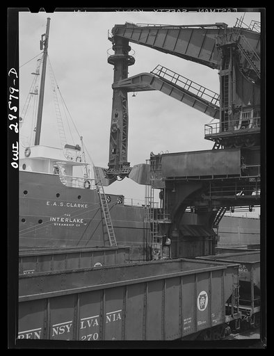 Cleveland, Ohio. Unloading a lake freighter at the Pennsylvania Railroad iron ore docks by means of Hewlett [i.e., Hulett] unloaders. In the foreground, empty cars are waiting to pass under the unloaders to pick up their loads