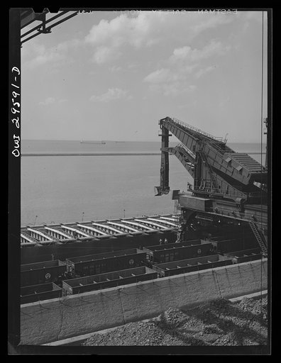 Untitled photo, possibly related to: Cleveland, Ohio. Unloading a lake freighter at the Pennsylvania Railroad iron ore docks by means of Hewlett [i.e., Hulett] unloaders. In the foreground, empty cars are waiting to pass under the unloaders to pick up their loads