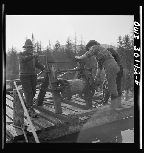 Spring pulpwood drive on the Brown Company timber holdings in Maine. Woodsmen winching up the boom on Long Pond; during the night the wind has blown the logs in the boom up pond away from the dam through which they must be sluiced