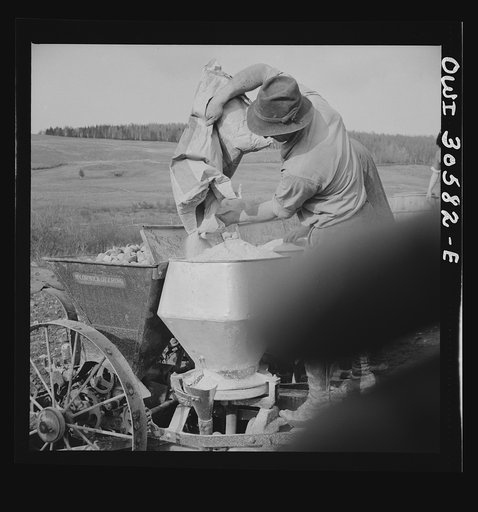 Untitled photo, possibly related to: Fort Kent, Aroostook County, Maine. Spring potato planting on the French Acadian farm of Leonard Gagnon. Leonard Gagnon loading fertilizer into the hopper of a seeder