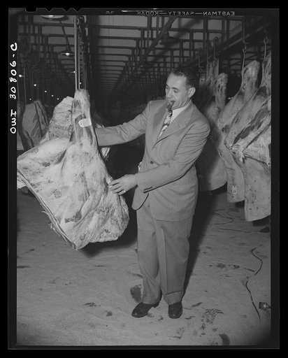 A man examining meat in a wholesale meat market. A reconstruction photographed during the filming of "Black Marketing," a motion picture produced by the U.S. Office of War Information (OWI)