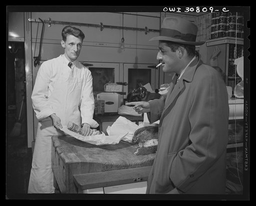 A patron talking to a butcher over the counter about some meat he is buying. A reconstruction photographed during the filming of "Black Marketing," a motion picture produced by the U.S. Office of War Information (OWI)