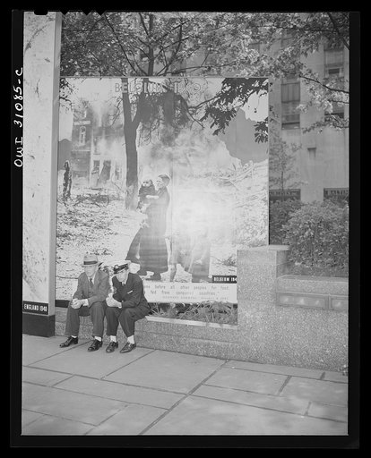 New York, New York. Men resting in front of the murals at the Nature of the Enemy exhibition, designed by the OWI (Office of War Information) and installed on the plaza of Rockefeller Center