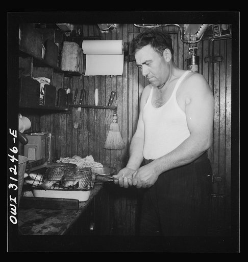 On board the fishing boat Alden, out of Gloucester, Massachusetts. Ship's cook preparing to broil freshly-caught mackerel for supper