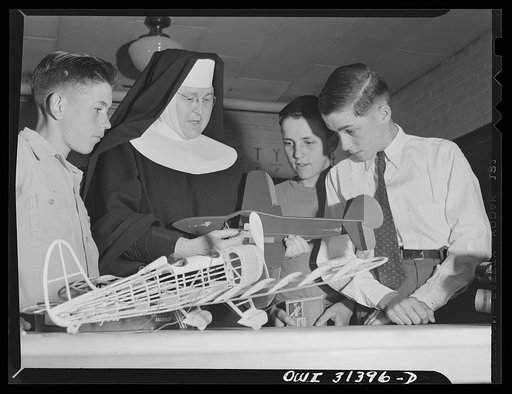 Untitled photo, possibly related to: Washington, D.C. Sister Aquinas, "flying nun," applying a little glue to the model P-38 which hangs from the ceiling of her classroom at Catholic University. A veteran of fifteen years' teaching experience, the Sister is giving a summer Civil Aeronautics Authorit