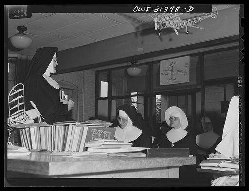 Untitled photo, possibly related to: Washington, D.C. Sister Aquinas, "flying nun," applying a little glue to the model P-38 which hangs from the ceiling of her classroom at Catholic University. A veteran of fifteen years' teaching experience, the Sister is giving a summer Civil Aeronautics Authorit