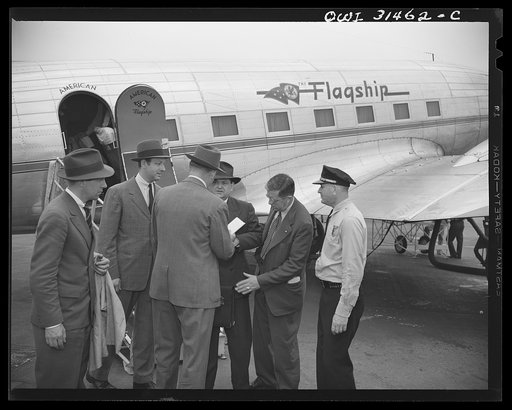 An officer and a government official (?) meeting two men at the American Airlines "Flagship" passenger plane and examining the contents of a brief case, in a scene in the motion picture "Black Marketing," produced by the U.S. Office of War Information (OWI) and released August 19, 1943