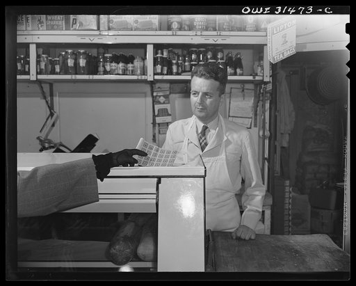 A butcher behind the counter over which a woman is handing him her ration book, a scene from "Black Marketing," a motion picture produced by the U.S. Office of War Information (OWI) and released August 19, 1943