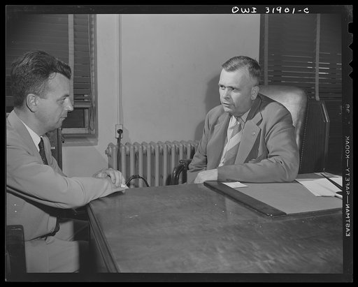 A government official(?) interviewing a man, in connection with a "black market" case. A reconstruction photographed during the filming of "Black Marketing," a motion picture produced by the U.S. Office of War Information (OWI)