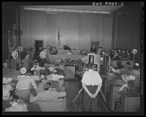 A courtroom scene, showing a photographer in the foreground, during the filming of "Black Marketing," a motion picture produced by the U.S. Office of War Information (OWI), and released August 19, 1943