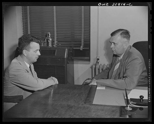 A government official(?) interviewing a man in connection with a "black market" case, a scene from "Black Marketing," a motion picture produced by the U.S. Office of War Information (OWI)