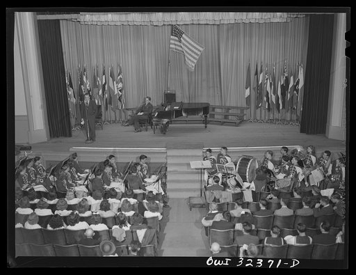 Oswego, New York. Howard Fast, author of Citizen Tom Paine, addressing the high school. United Nations flags are on the stage during United Nations week