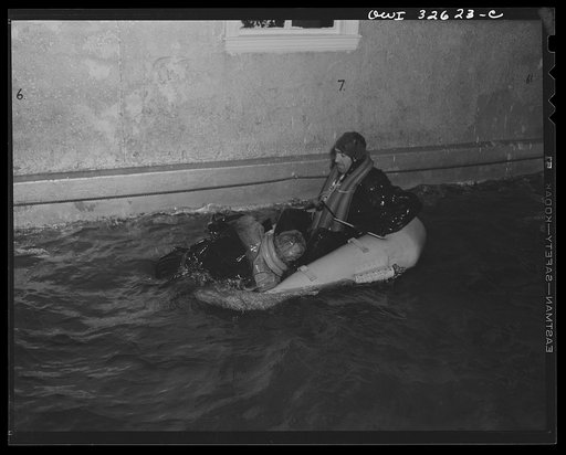 Untitled photo, possibly related to: Bar Harbor, Maine. Civil Air Patrol base headquarters of coastal patrol no. 20. A flyer in an all-rubber crash suit testing the use of a rubber boat, which he is extracting from its bag