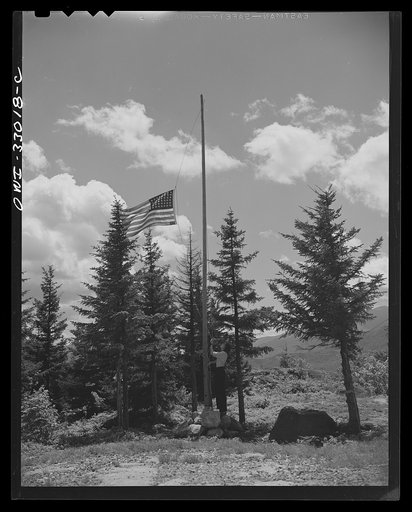 Gorham (vicinity), New Hampshire. Barbara Mortensen, a fire and airplane lookout on Pine Mountain, running up the colors
