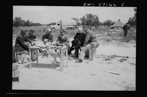 Archbishop Spellman of New York dining at a fighter base of the U.S. Army 9th Air Force somewhere in Tunisia. Left to right: Colonel C. M. Seabach, Adjutant General, U.S. Army 9th Air Force; Major G. T. Mullins; Colonel E. E. Bates; Brigadier General Auby C. Strickland; Archbishop Spellman; Captain 