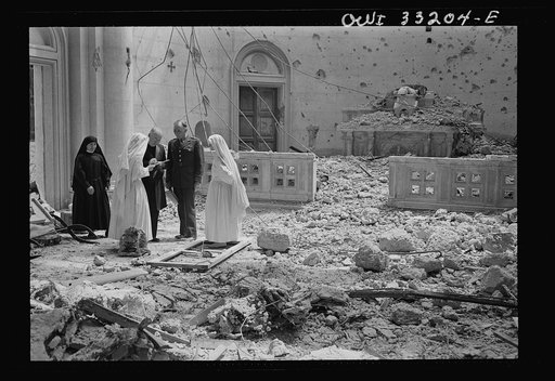 Tripoli, Libya. Archbishop Spellman of New York (left) surveys the ruins of the chapel of the Franciscan Missionaries of Mary. With him are Brigadier General Auby C. Strickland of the U.S. Army 9th Air Force and Catholic nuns