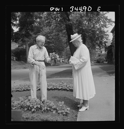 Oswego, New York. A citizen showing his wife vegetables from his victory garden as she starts on her way to church