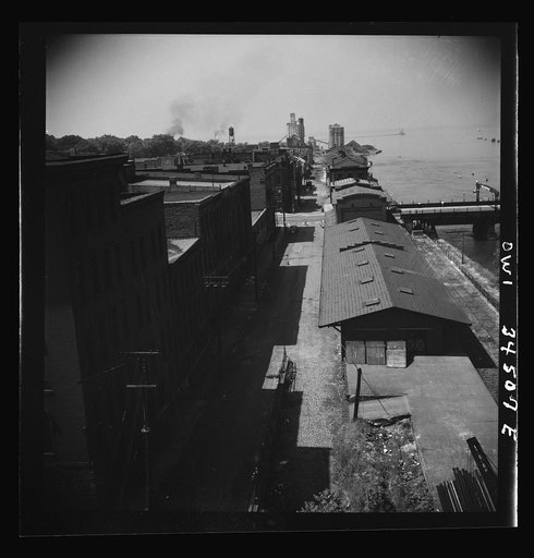 Untitled photo, possibly related to: Oswego, New York. The waterfront looking toward Lake Ontario. A grain elevator is in the far left and the bauxite docks are at the far right