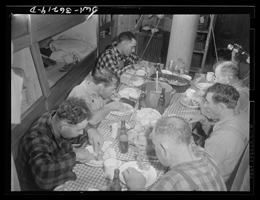 On board a fishing vessel out from Gloucester, Massachusetts. Crew eating in the forecastle. The one room serves as dining room, bedroom and kitchen. Between times the men use it for a game room, where they play cards and discuss politics