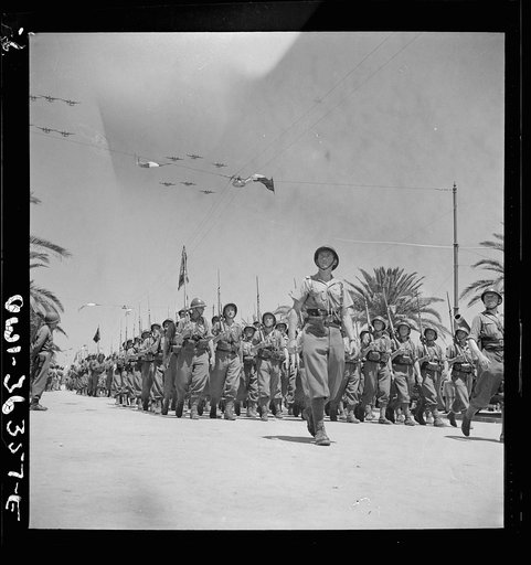 Tunis, Tunisia. French troops passing the reviewing stand in the Allied victory parade along Avenue Gambetta as American planes fly overhead in a show of Allied might