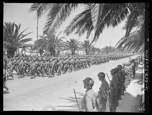Tunis, Tunisia. French soldiers marching in the Allied parade along Avenue Gambetta. American soldiers standing at parade rest in the foreground