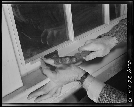 Washington, D.C. Installing a "Victory" storm pane, or extra pane of glass on a home window as a war-time fuel conservation measure. Fastening a three inch strip of molding to the lower frame of the window