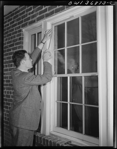 Washington, D.C. Installing a "Victory" storm pane, or extra pane of glass on a home window as a war-time fuel conservation measure. Entire perimeter of the victory storm pane with all-weather sealing tape