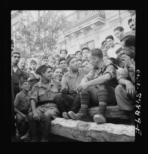 French-Canadian troops in Sicily, with French speaking Italians. The Italian soldier (center) is a veteran of many Italian engagements and is now a member of a local fire fighting outfit in a small village