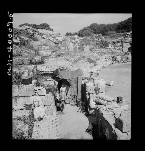 During the first few days after the Germans had been driven from Sicily, the people were obliged to live in makeshift homes, such as this ancient Roman amphitheatre. Now they are returning to their own homes, rebuilding, refurbishing, and starting life anew