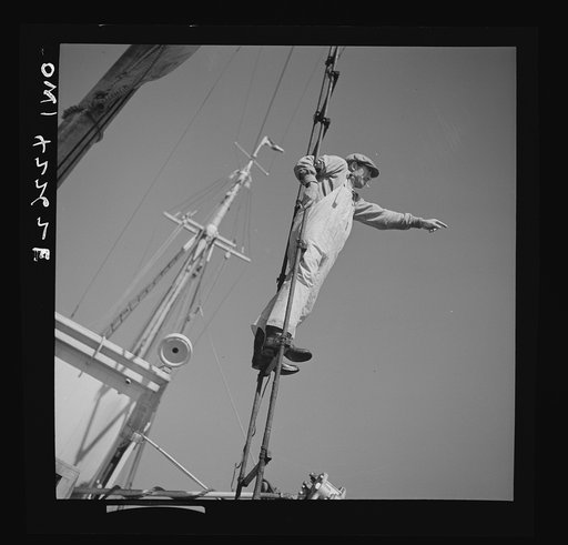 Gloucester, Massachusetts. A lookout climbs the cables high above "Old Glory's" deck to check the location of other trawlers. When one trawler strikes good fishing ground the captain notifies other boats in the fleet