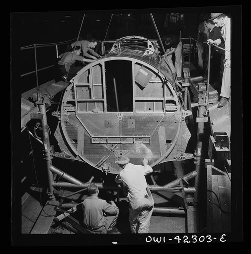 Seattle, Washington. Boeing aircraft plant. Production of B-17F (Flying Fortress) bombing planes. A complete fuselage section is being hoisted from its cradle in rope slings for mating with wing sections