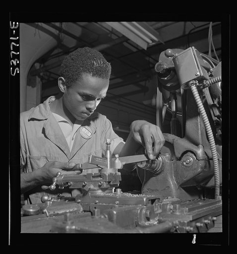 NYA (National Youth Administration) work center, Brooklyn, New York. A Negro bench-lathe worker, who is receiving training in machine shop practice, shown here removing a burr from a screw held in a collet