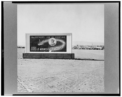 Las Vegas, Nevada. A billboard on the grounds of the gigantic plant of  Basic Magnesium Incorporated, showing tracer bullets and reading "MacArthur's job is fighting. OURS is magnesium." In the background can be seen workers' automobiles and some of the eighty-four foot silos and buildings of the pl
