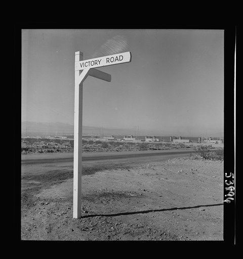 Las Vegas, Nevada. A crossroad sign reading "Victory Road," with buildings, storage silos and transmission lines of the Basic Magnesium Incorporated plant in the background
